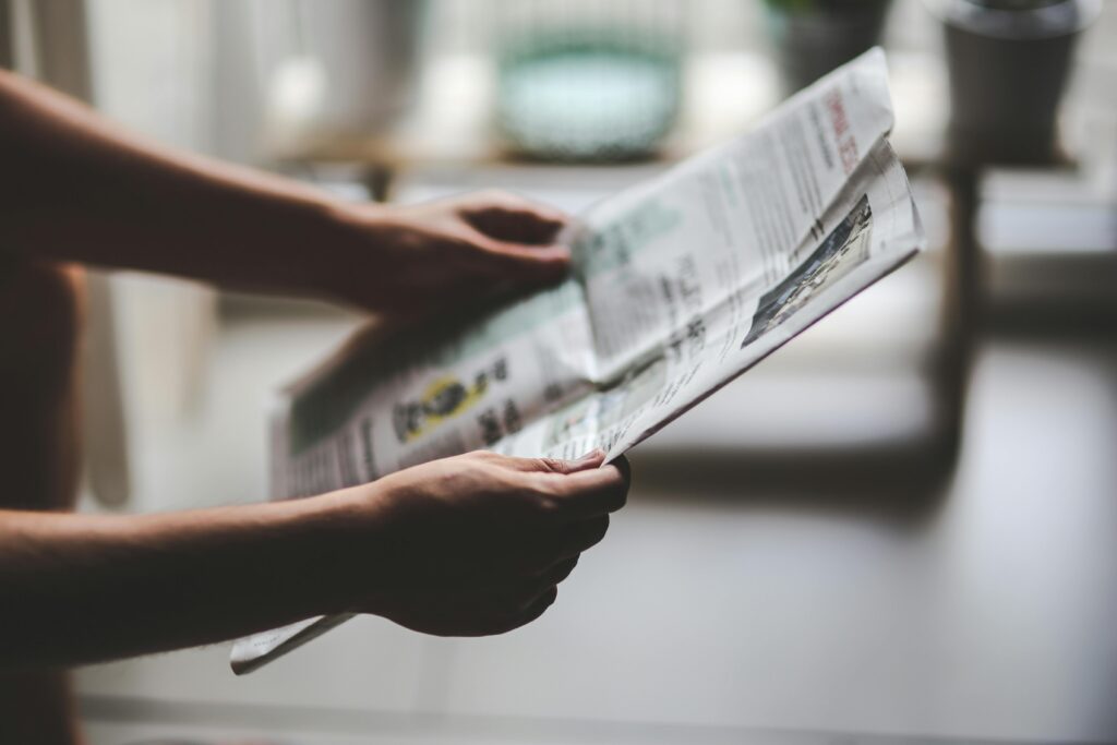 Hands holding a newspaper in a soft-lit, indoor environment, focusing on a relaxed reading moment.